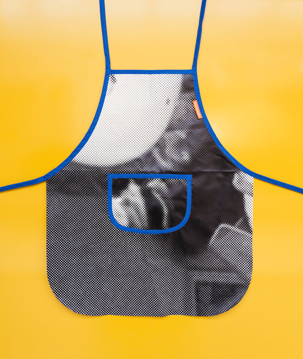 Die kleine Schürze mit Brusttasche liegt plan auf einem gelben Hintergrund
