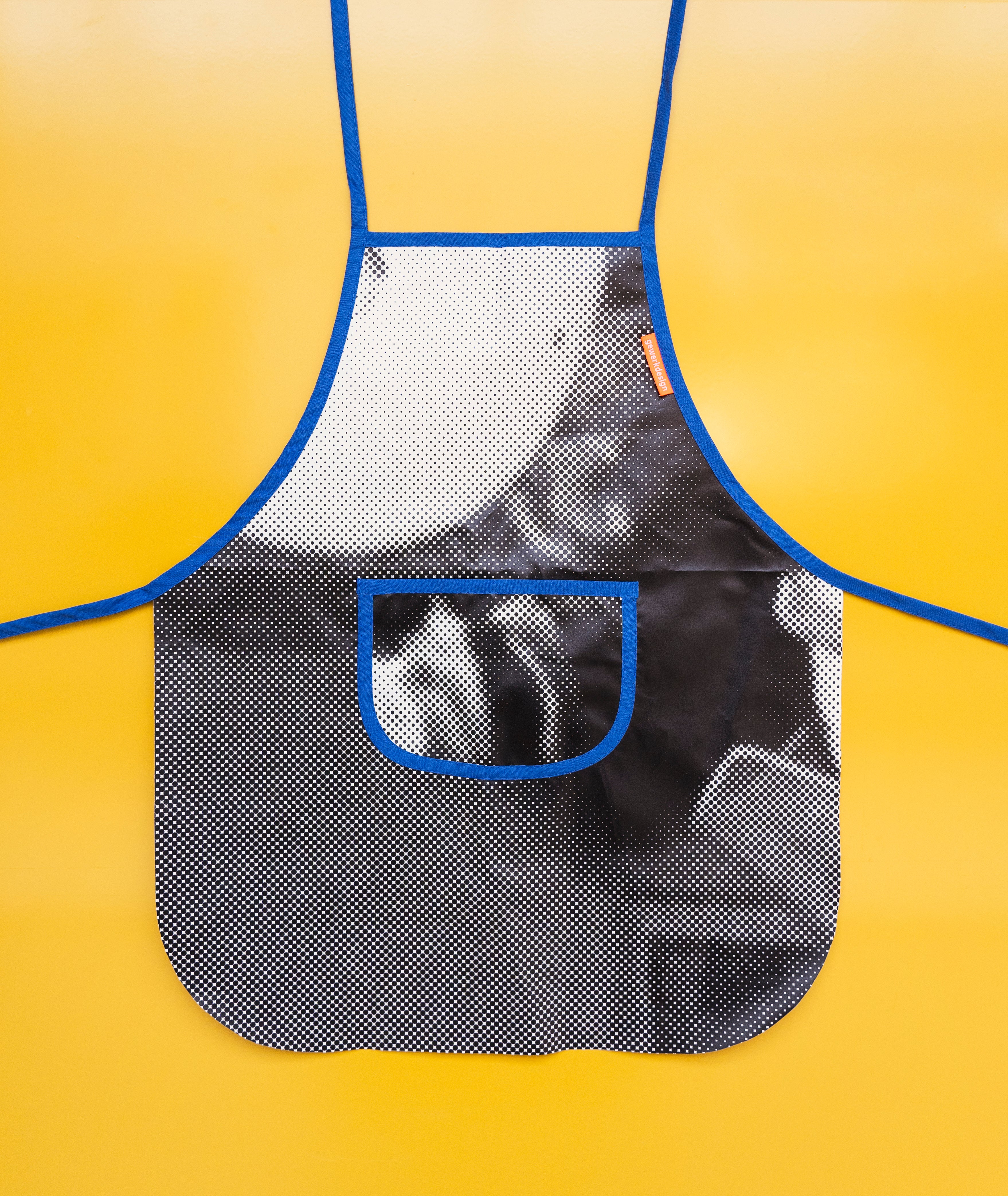 Die kleine Schürze mit Brusttasche liegt plan auf einem gelben Hintergrund